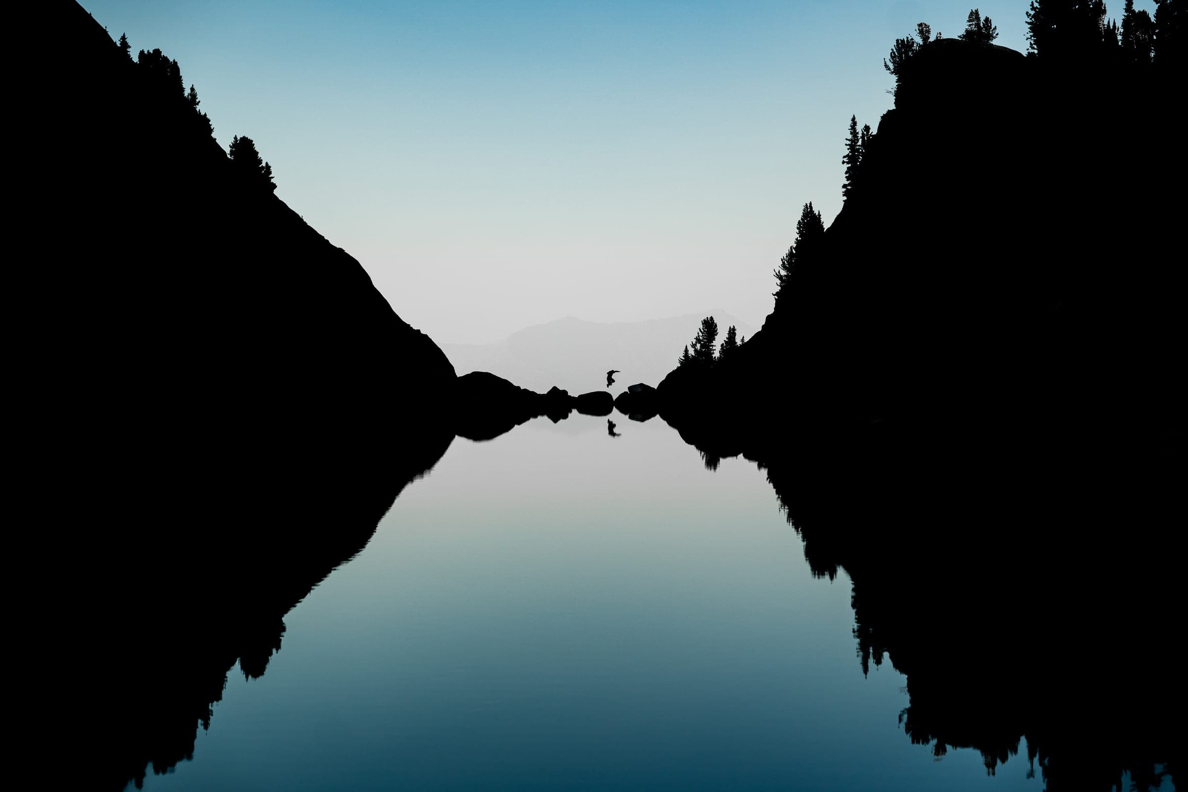 Mirror-lake silhouette with tiny figure at the seam
