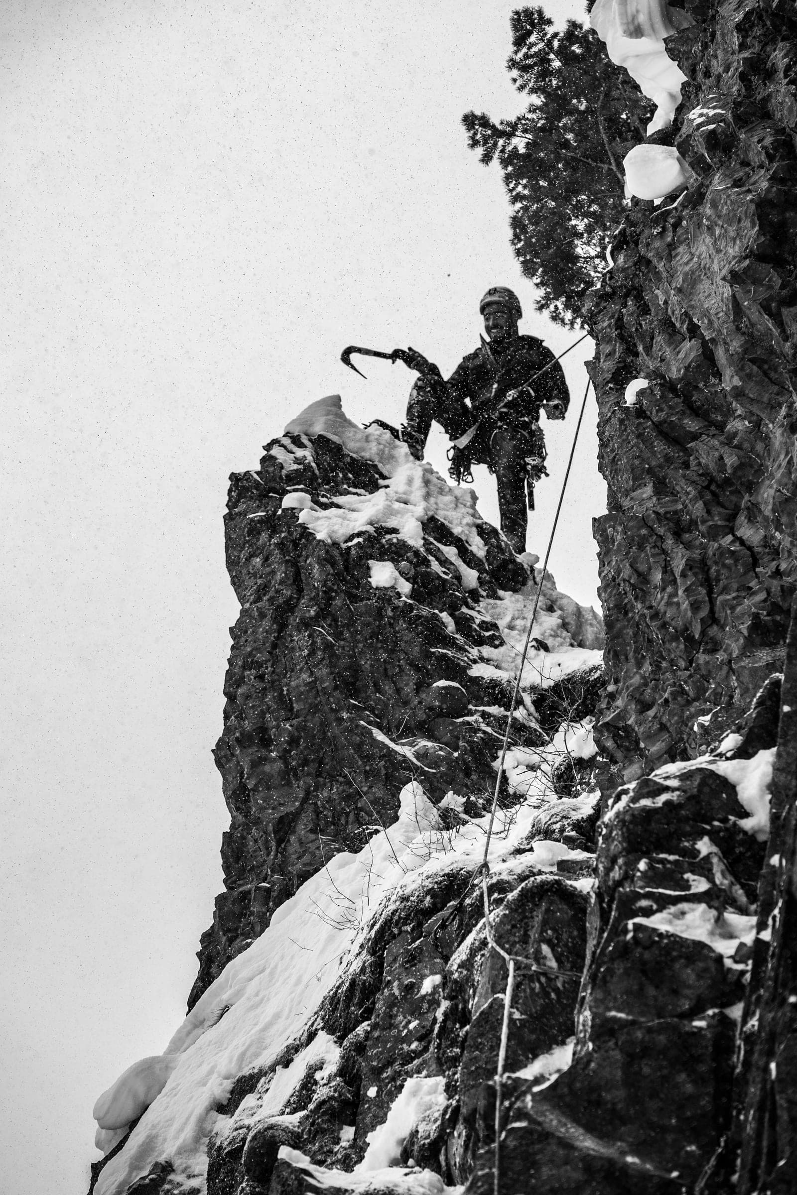 B&W climber topping out a snowy pinnacle against white sky