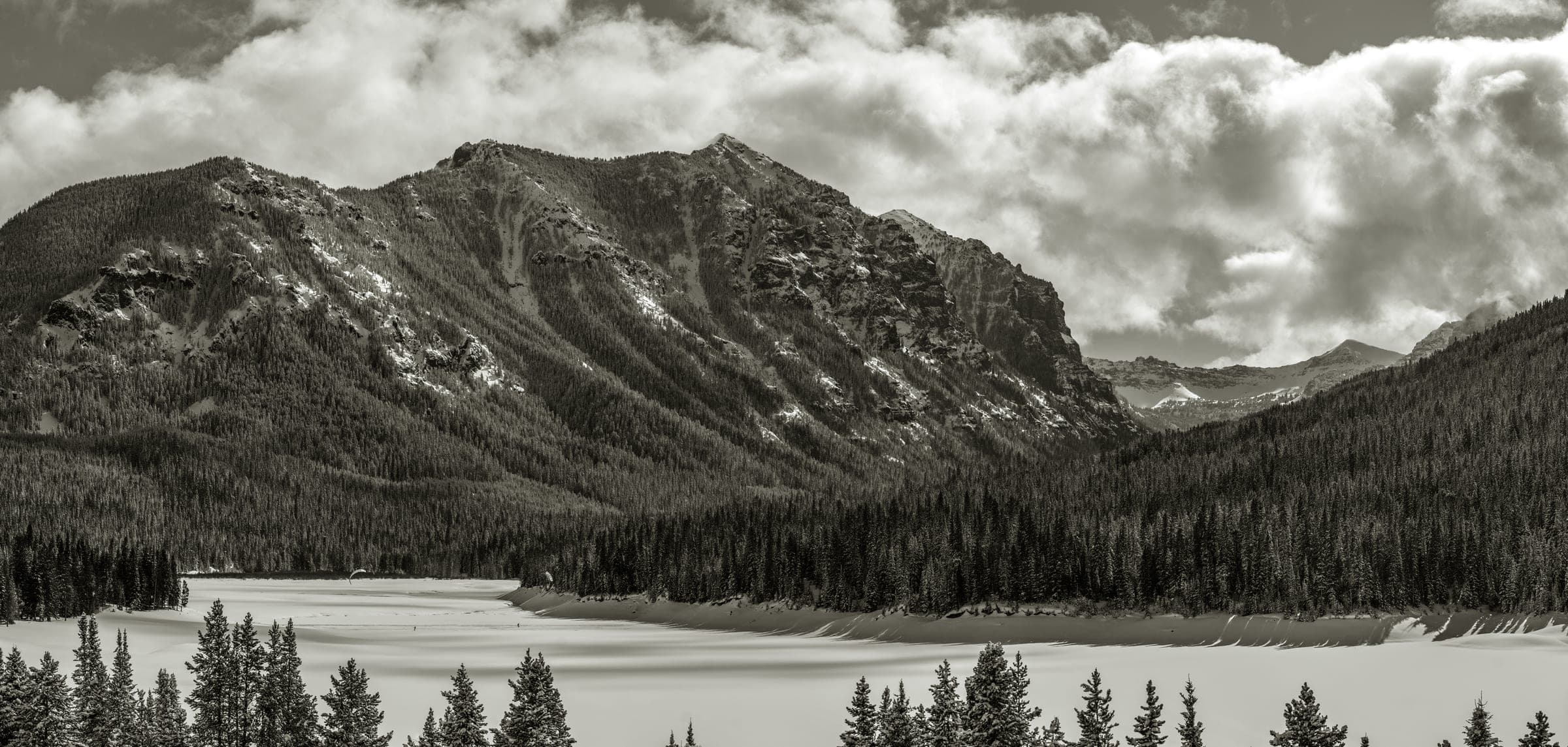 B&W panorama of a peak and frozen lake under heavy clouds