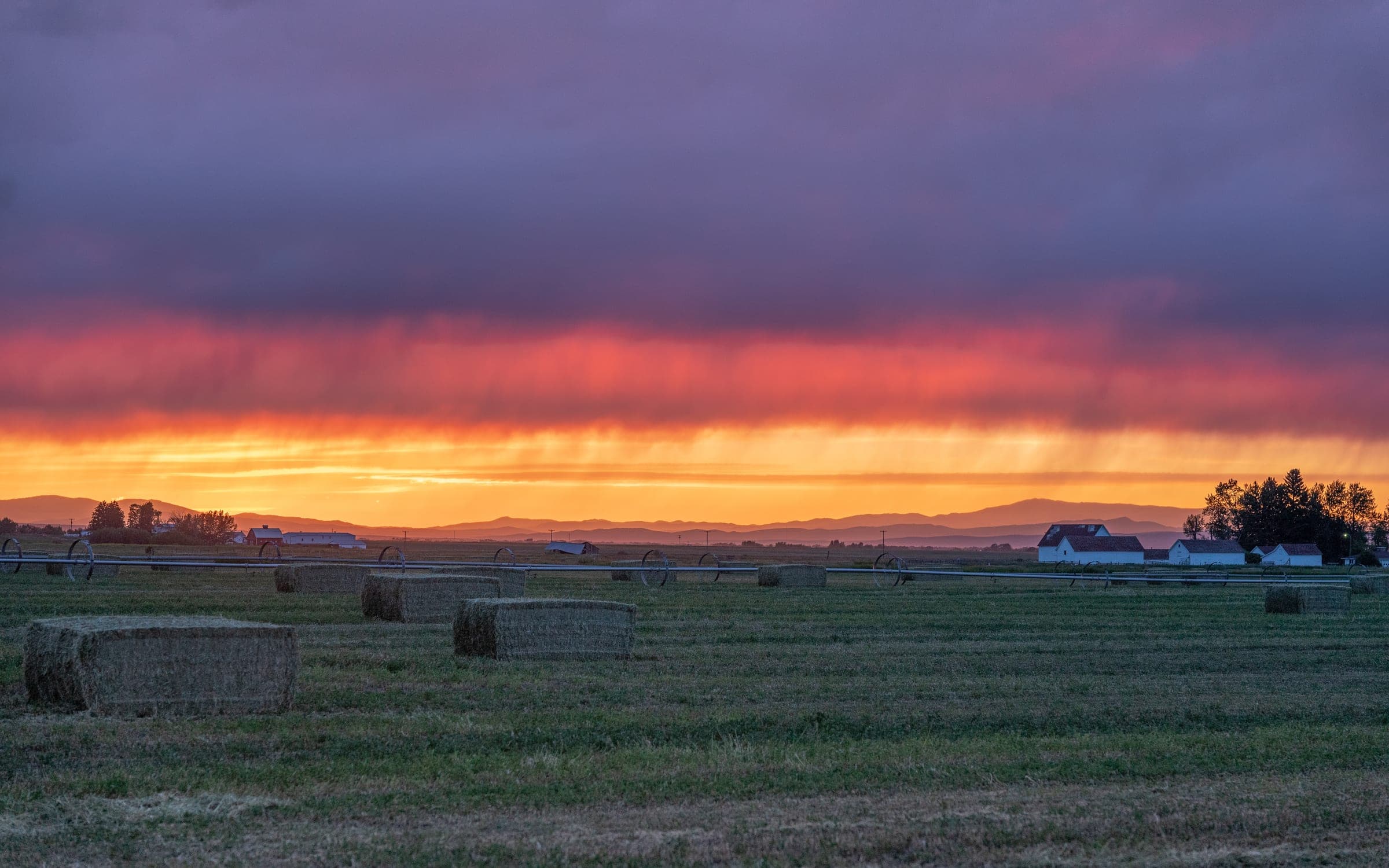 Fiery sunset over hay bales and a farmhouse
