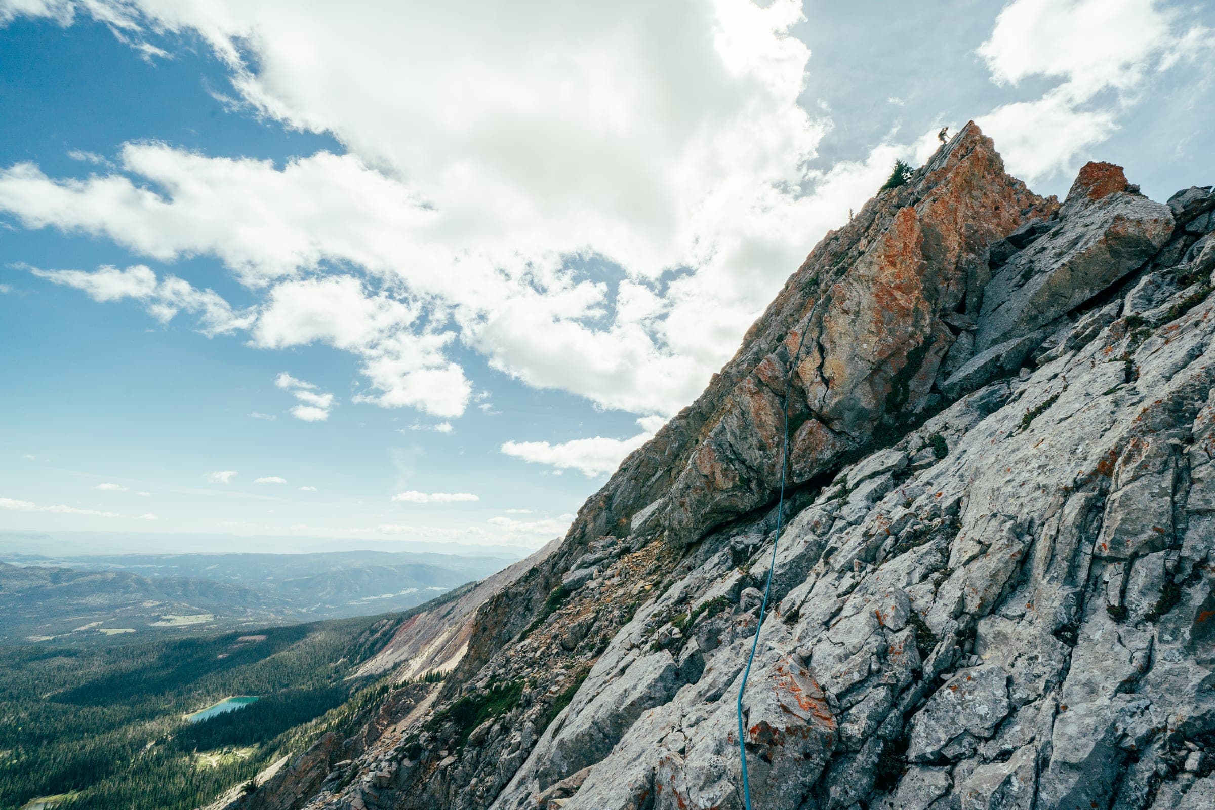 Climber high on the orange Bone Saw ridge under big clouds, Sacagawea
