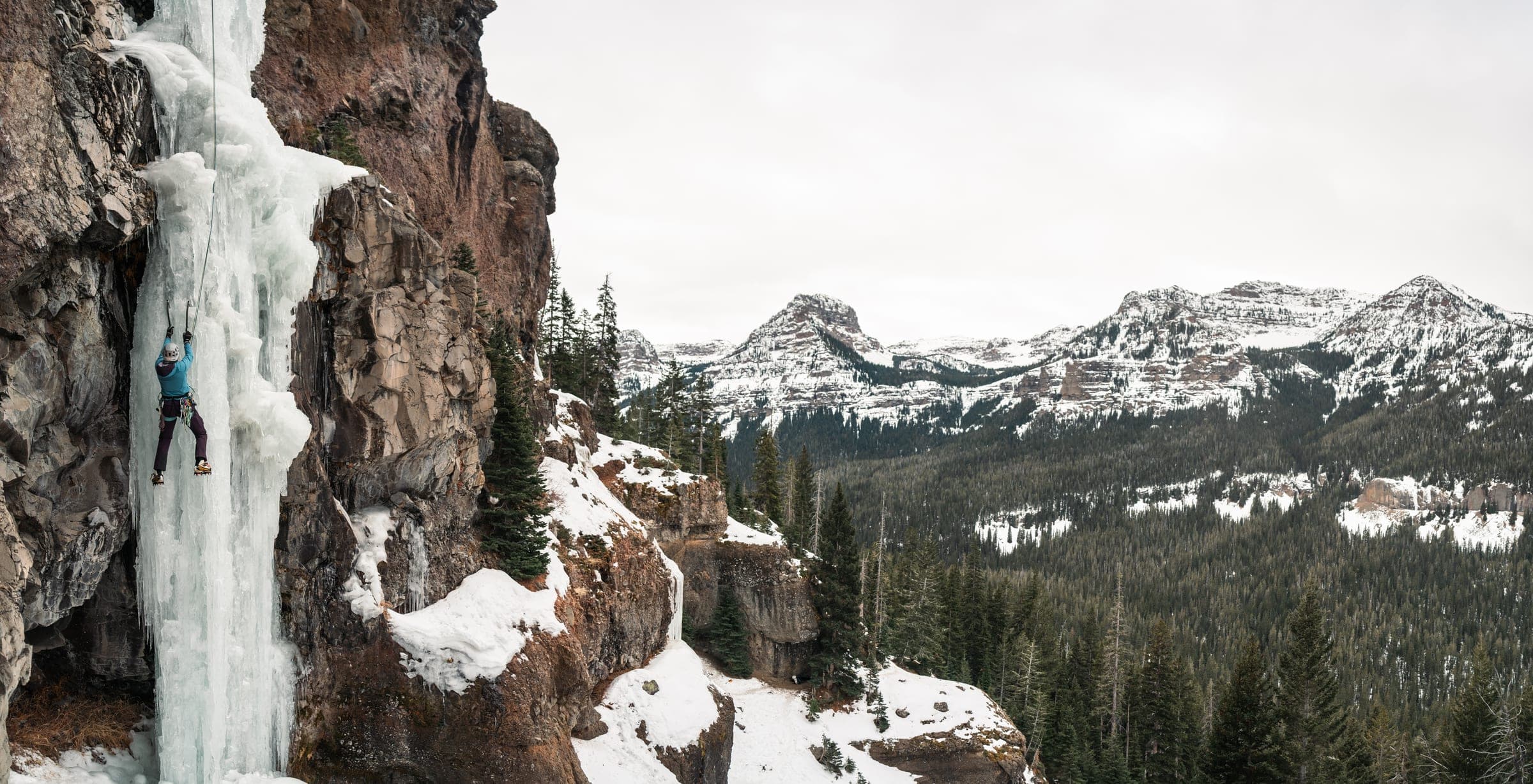 Ice climber on a frozen pillar above snowy peaks