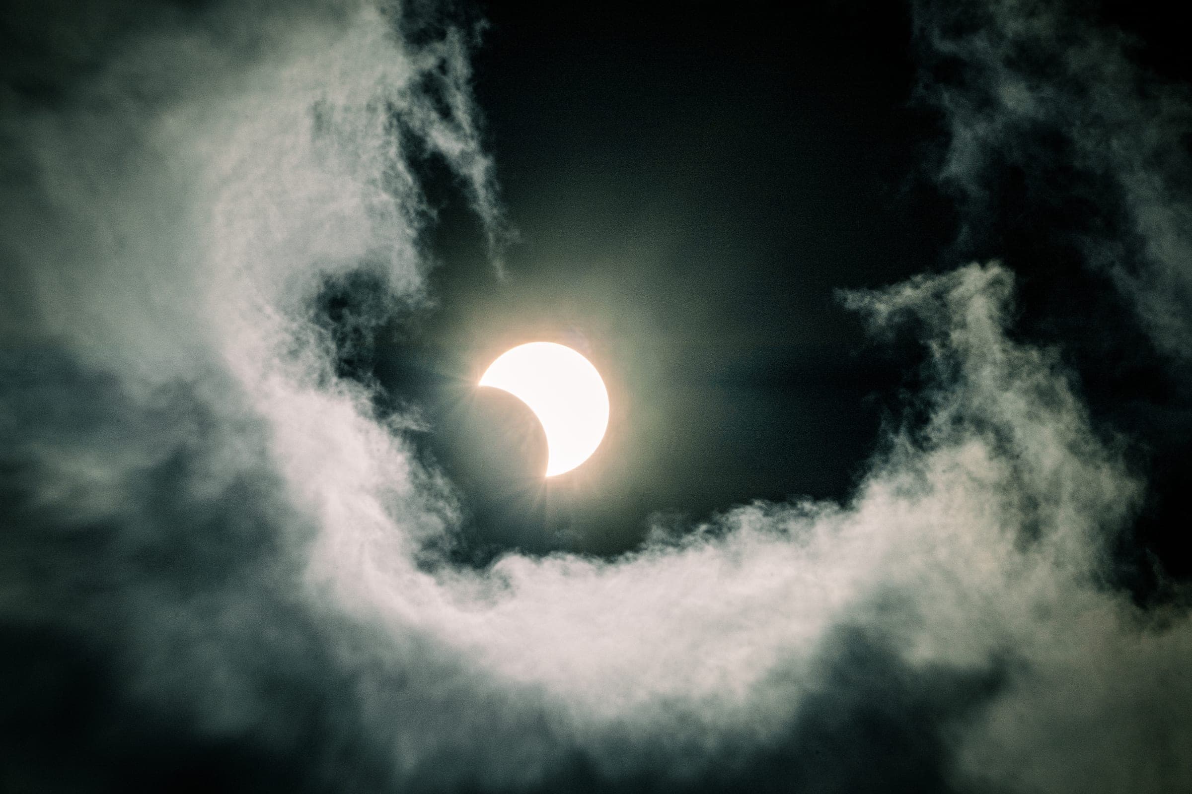 Partial solar eclipse ringed by swirling clouds