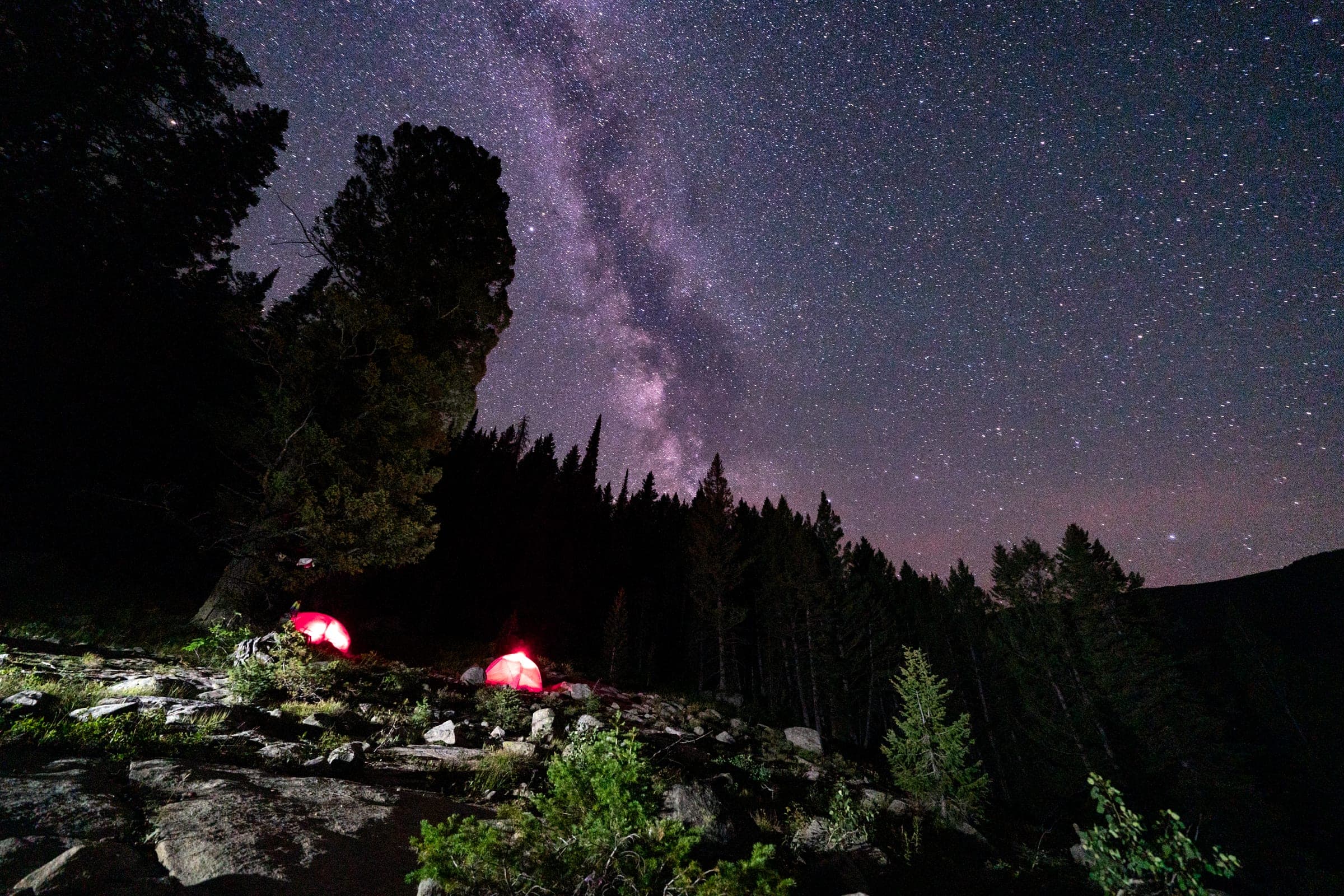 Milky Way over glowing tents beneath a rock pillar