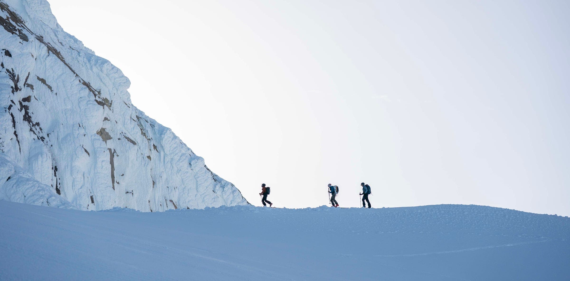Three climbers on a stark snow ridge under pale sky