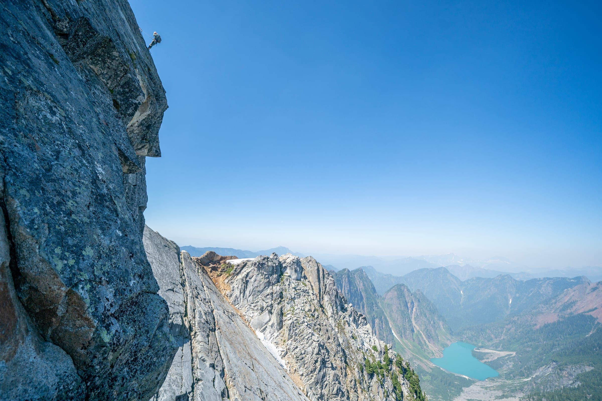 Climber on a sheer wall above a turquoise alpine lake
