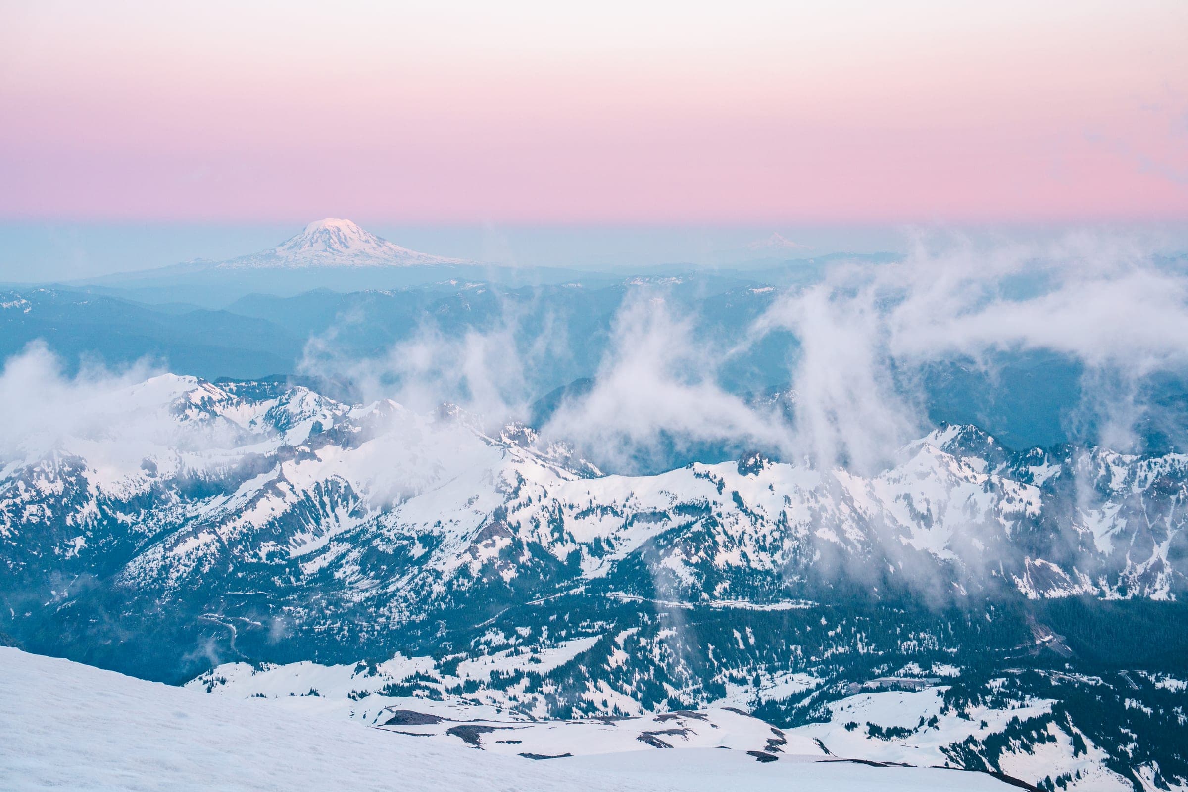 Clouds pouring through Tatoosh peaks under pink sky with Adams beyond