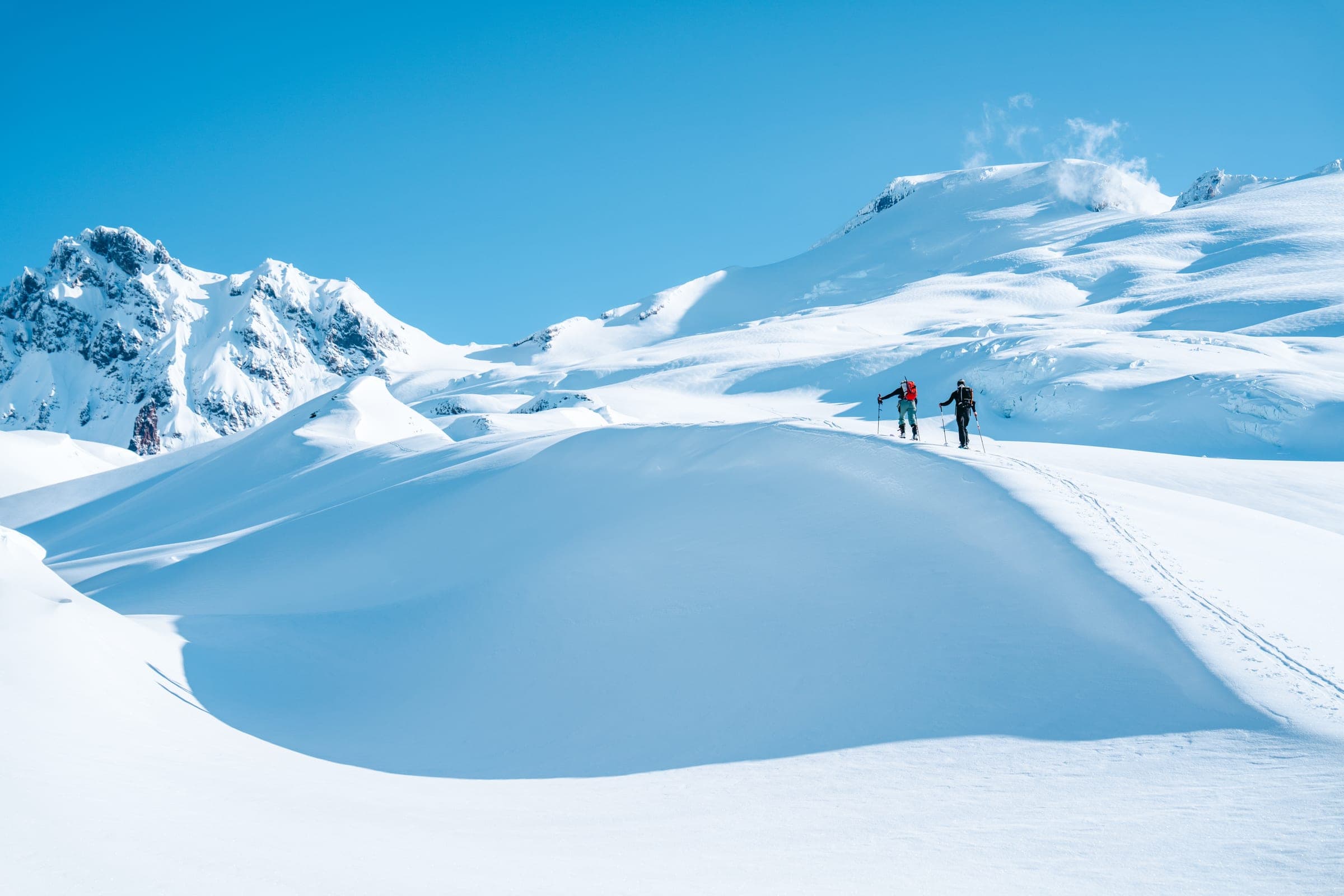 Two skiers crossing a sculpted snow dome under Baker