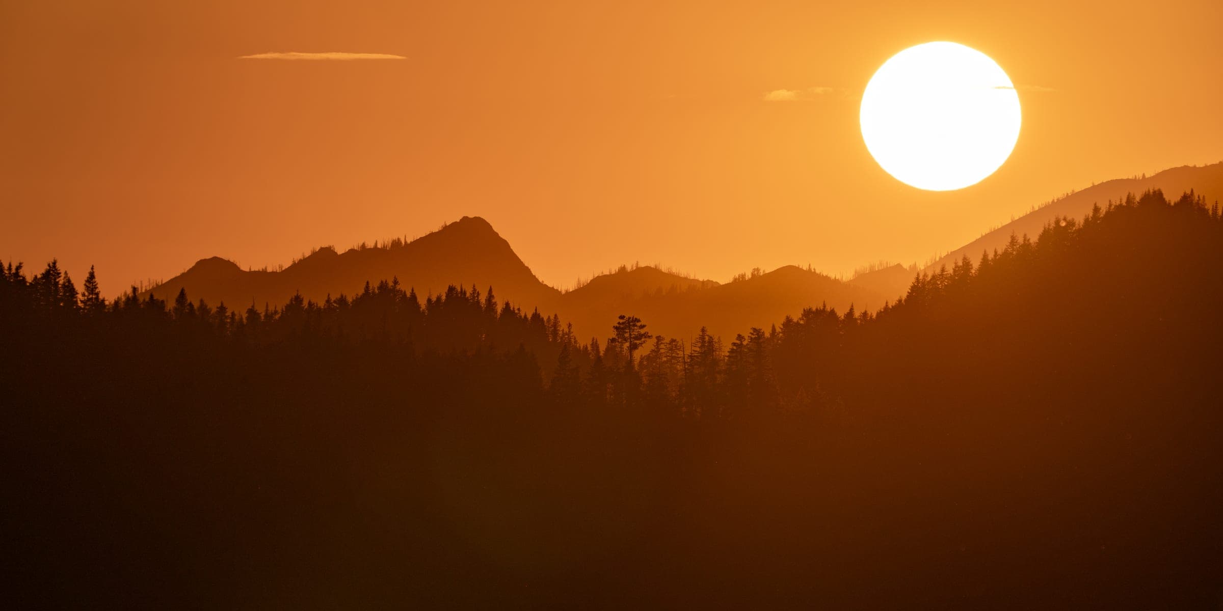Orange sun setting over layered ridge silhouettes