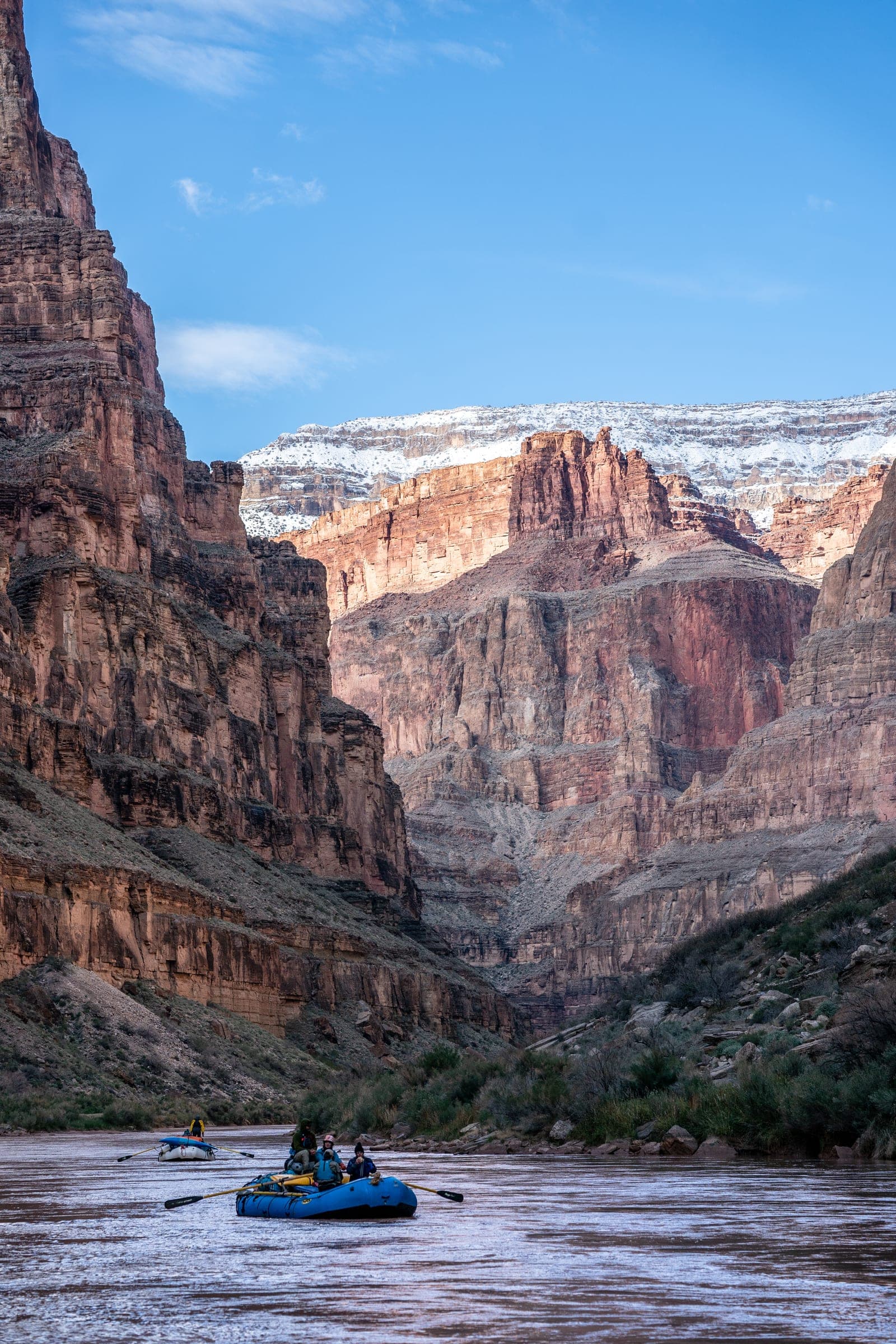 Raft beneath towering Grand Canyon walls with snow on the rim