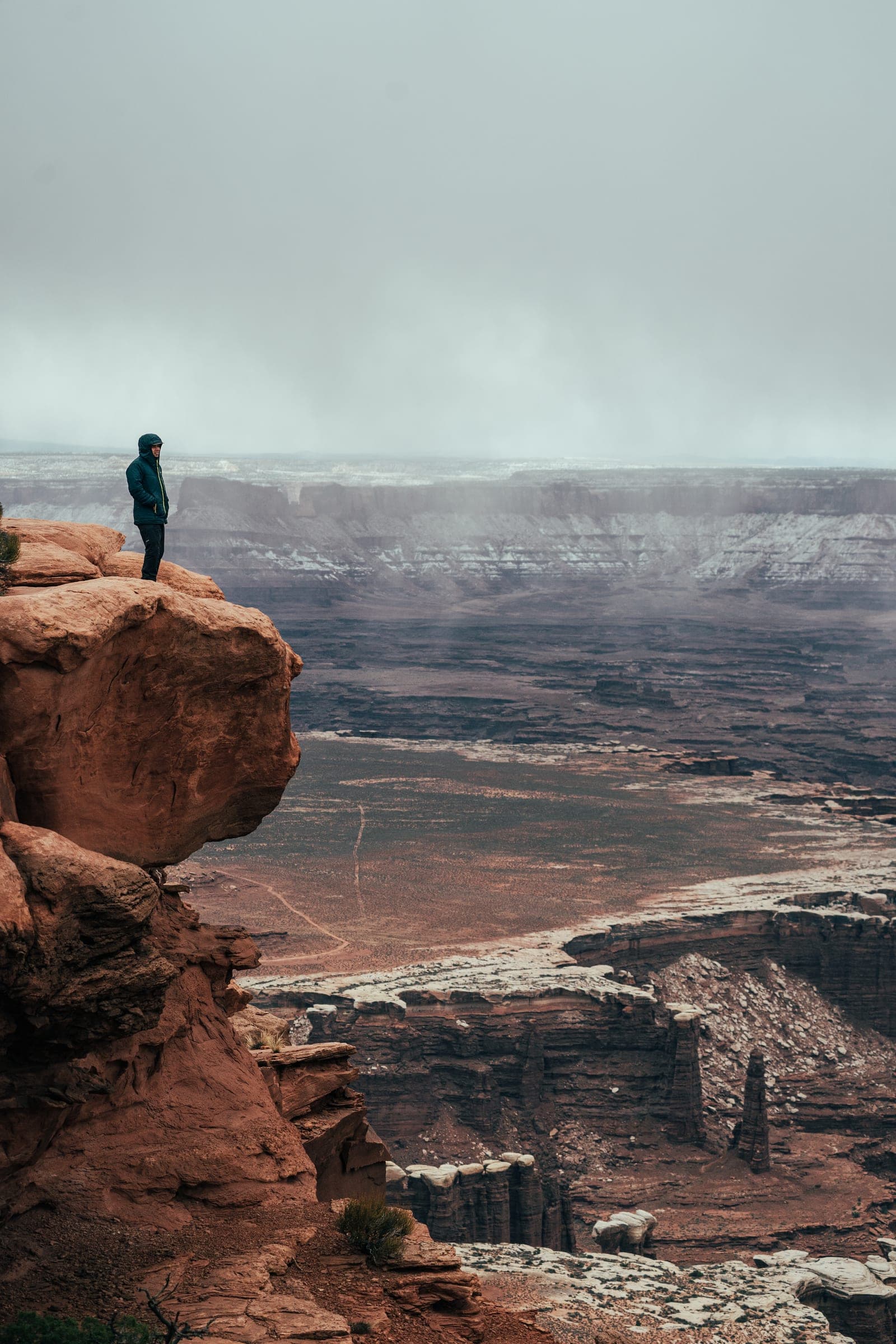 Figure on the rim above misty Canyonlands, vertical
