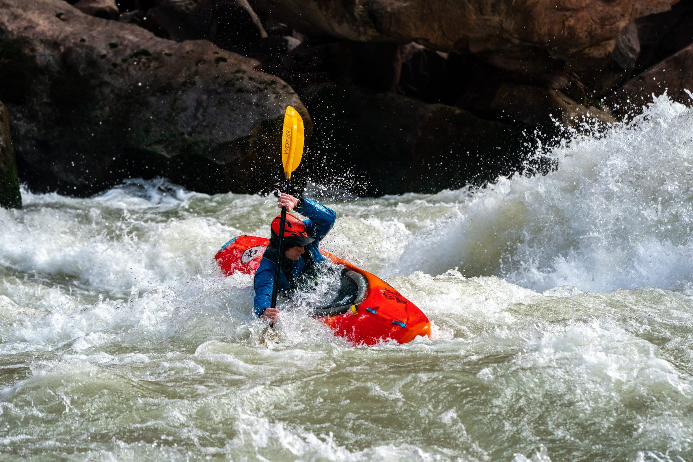 Whitewater kayaker punching a red-rock wave