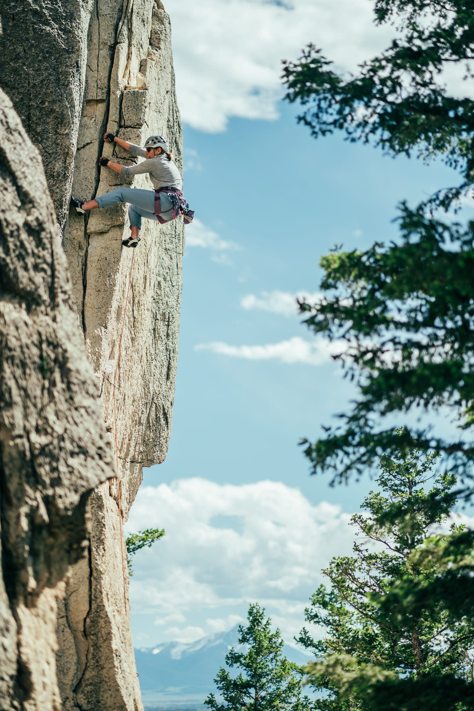 Climber laybacking a granite pillar against blue sky and pines, Allenspur