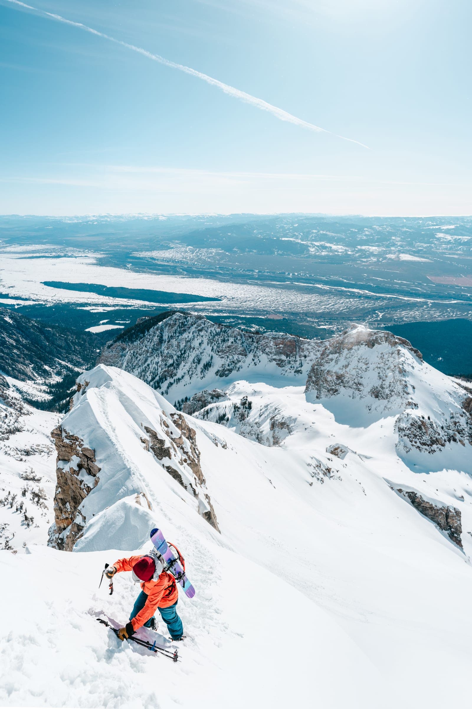 Climber in orange heading up a snowy couloir, tall vertical panorama