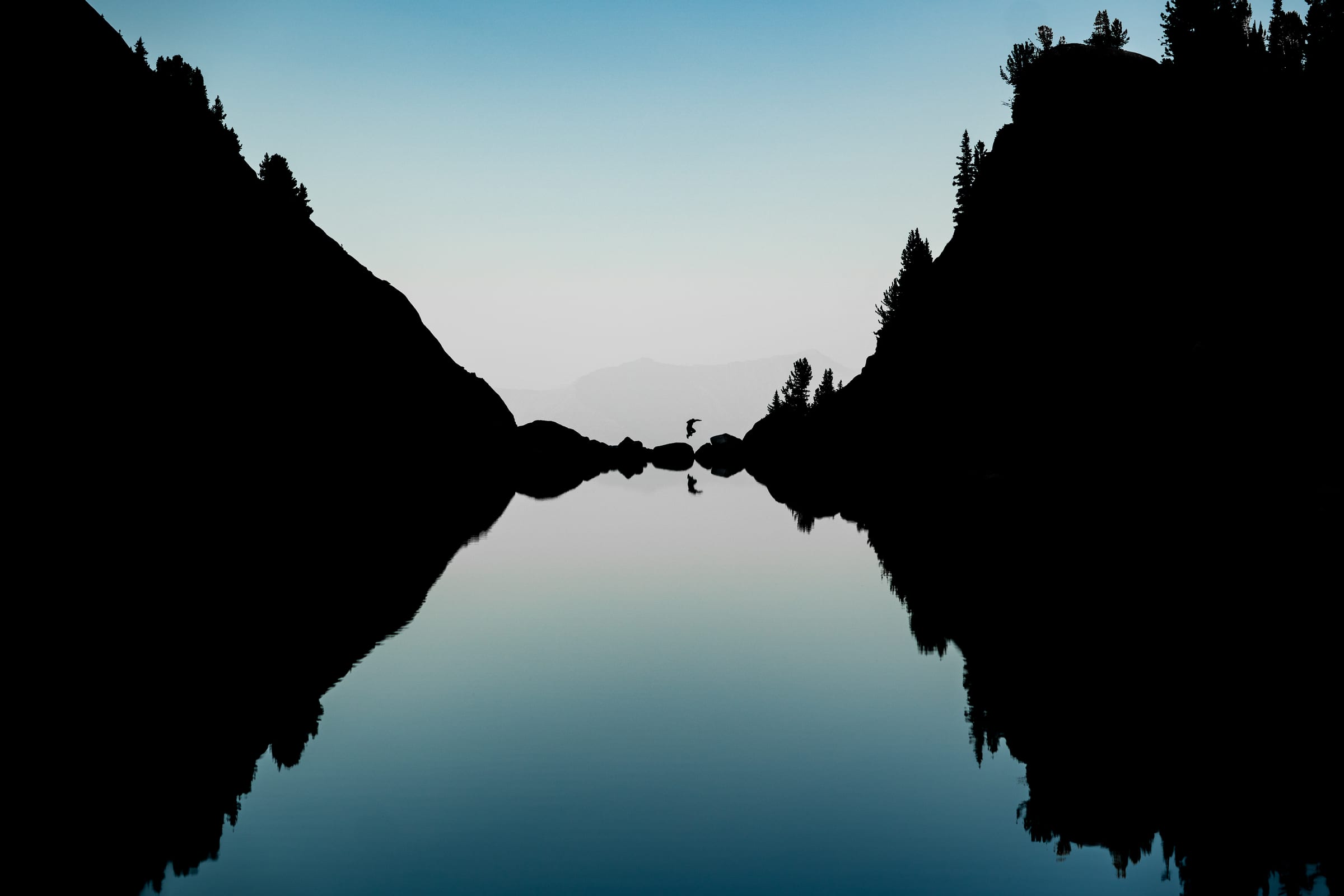 Mirror-lake silhouette with tiny figure at the seam