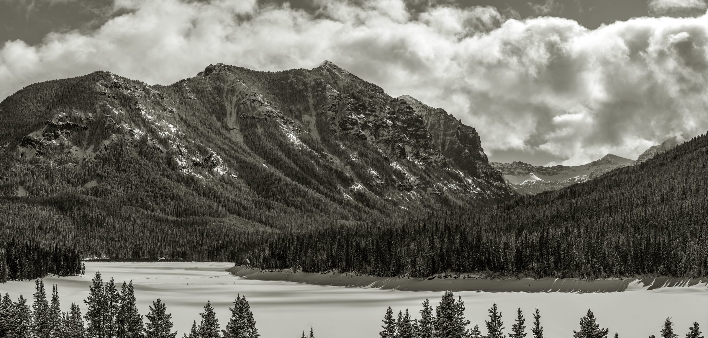 B&W panorama of a peak and frozen lake under heavy clouds
