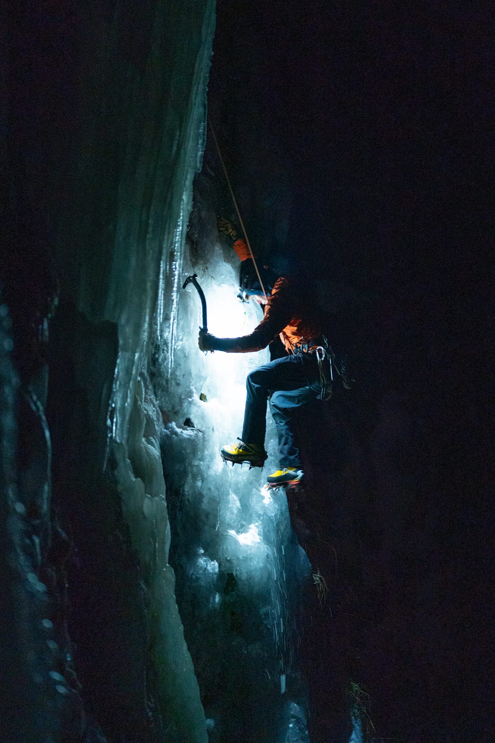 Night ice climbing in Hyalite, headlamp lighting a blue ice curtain