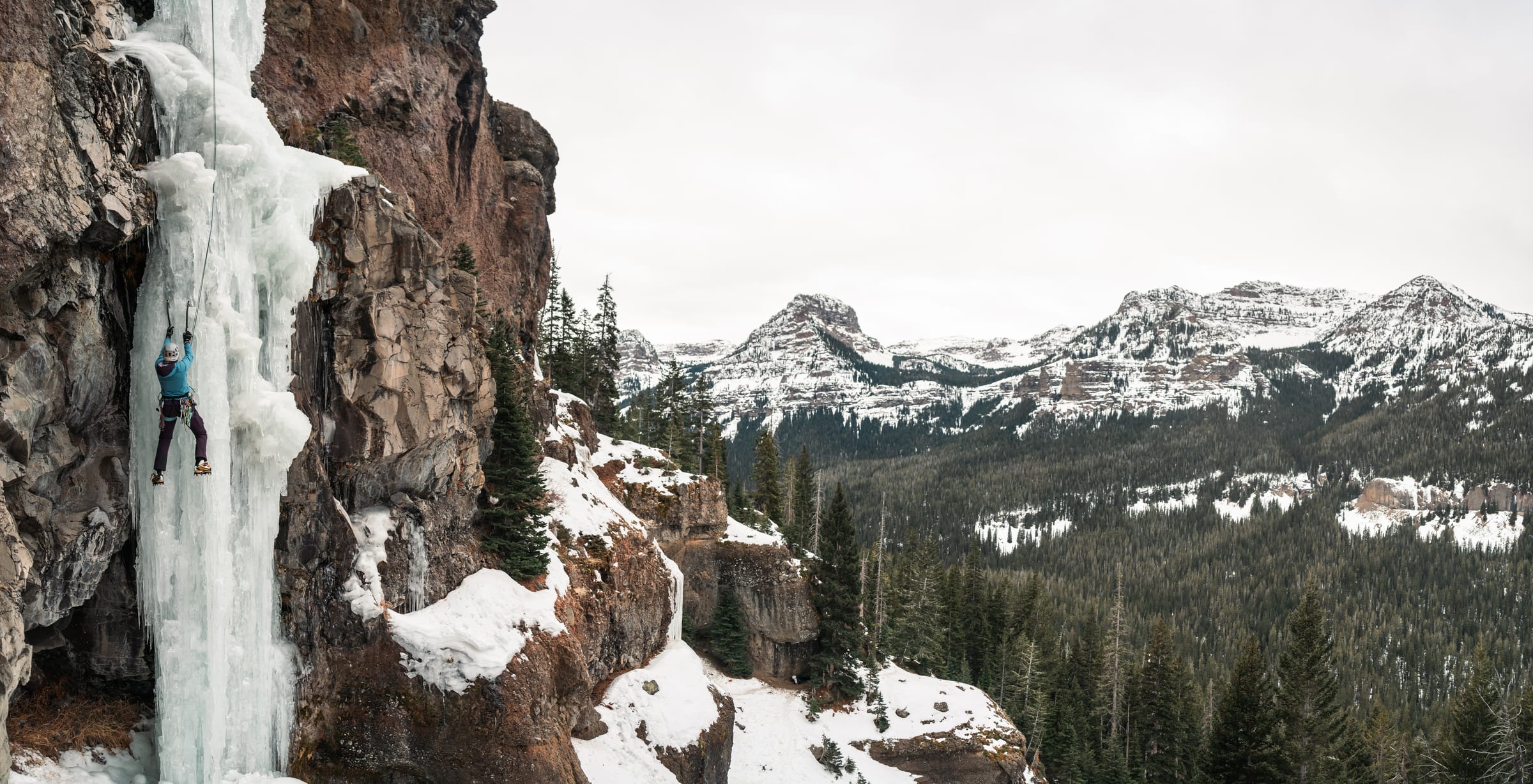 Ice climber on a frozen pillar above snowy peaks
