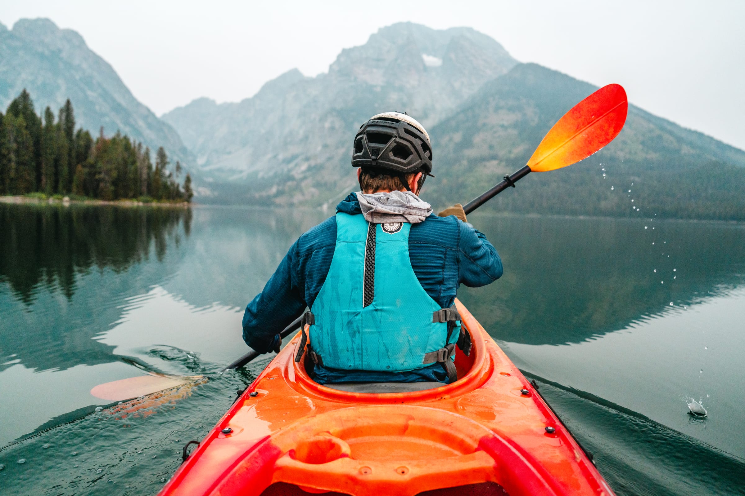 Over-the-shoulder kayak on a glassy Teton lake
