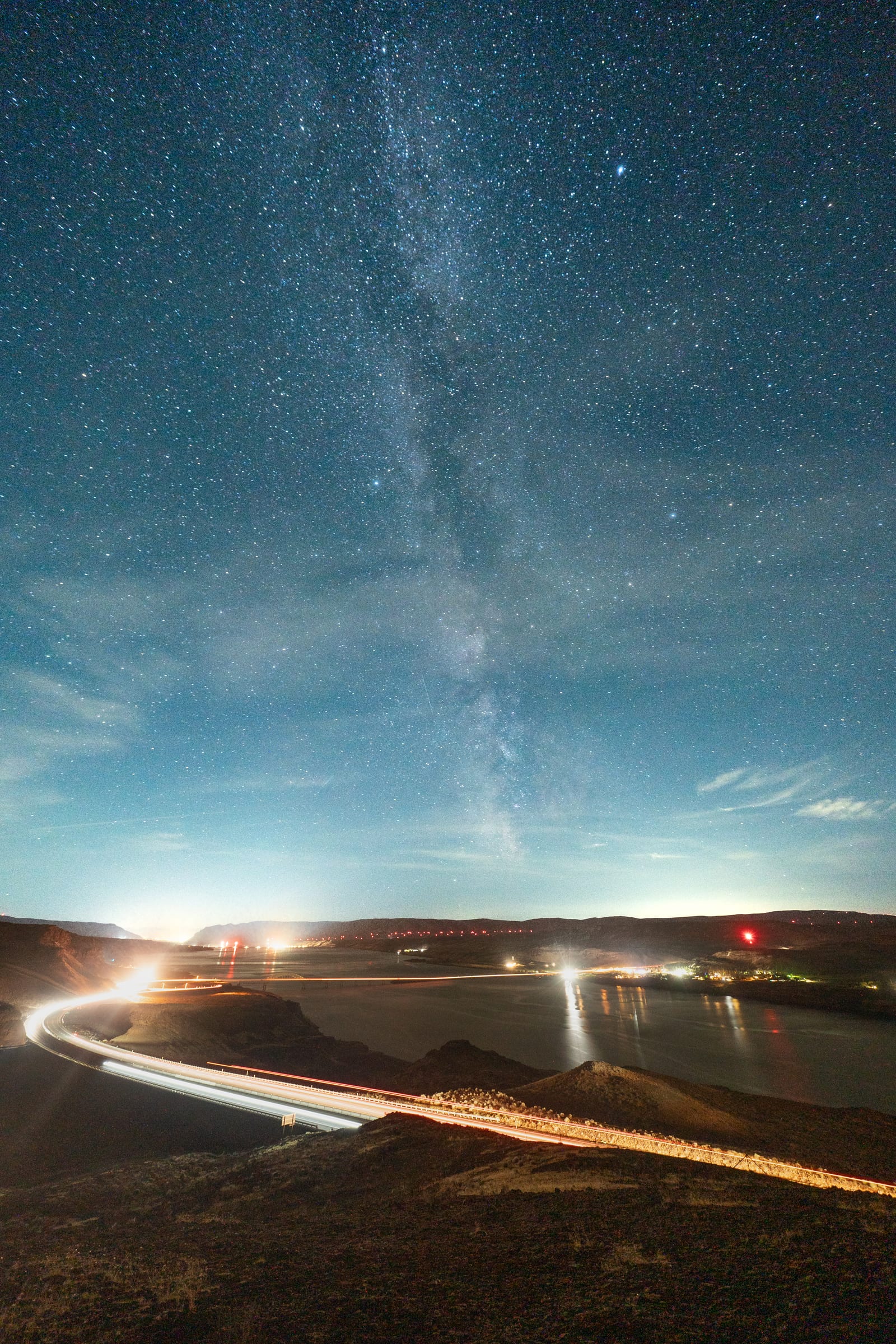 Milky Way over headlight trails curving along a lakeshore road