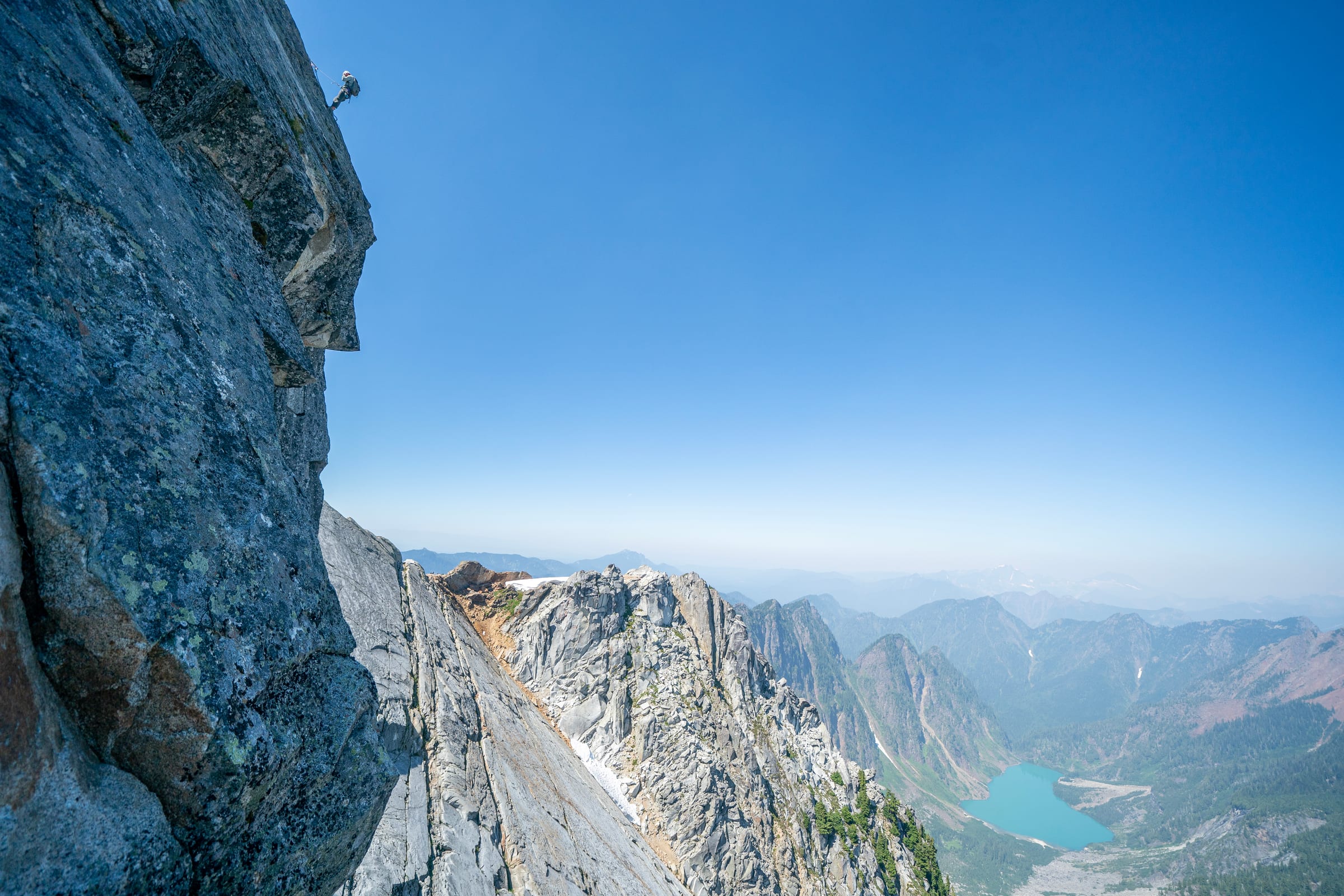 Climber on a sheer wall above a turquoise alpine lake