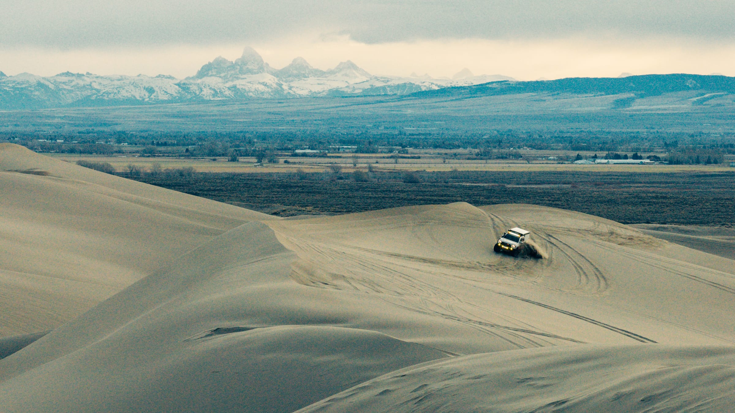 Truck cresting golden dunes with the Tetons on the horizon