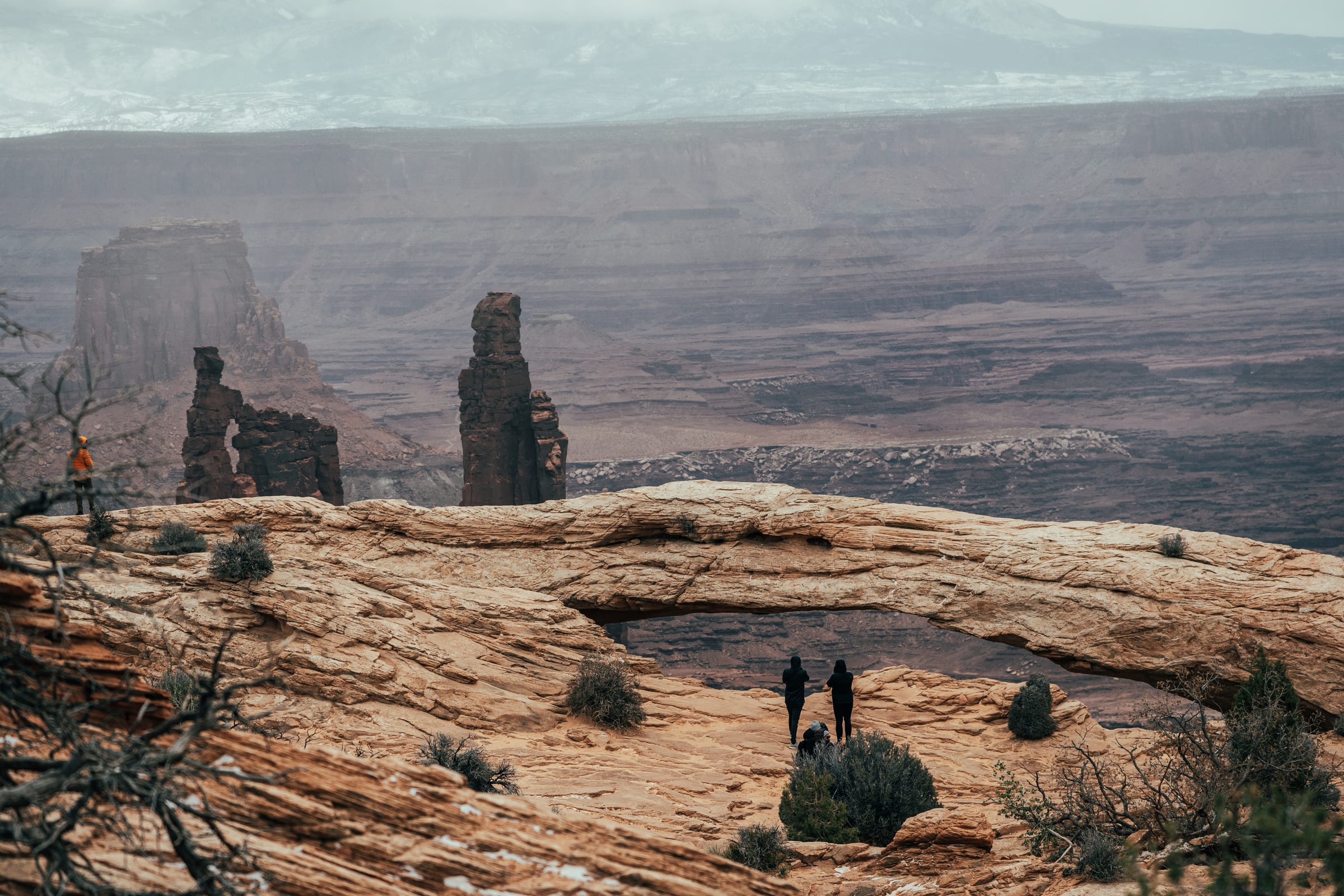 Mesa Arch framing storm-wrapped spires with two figures