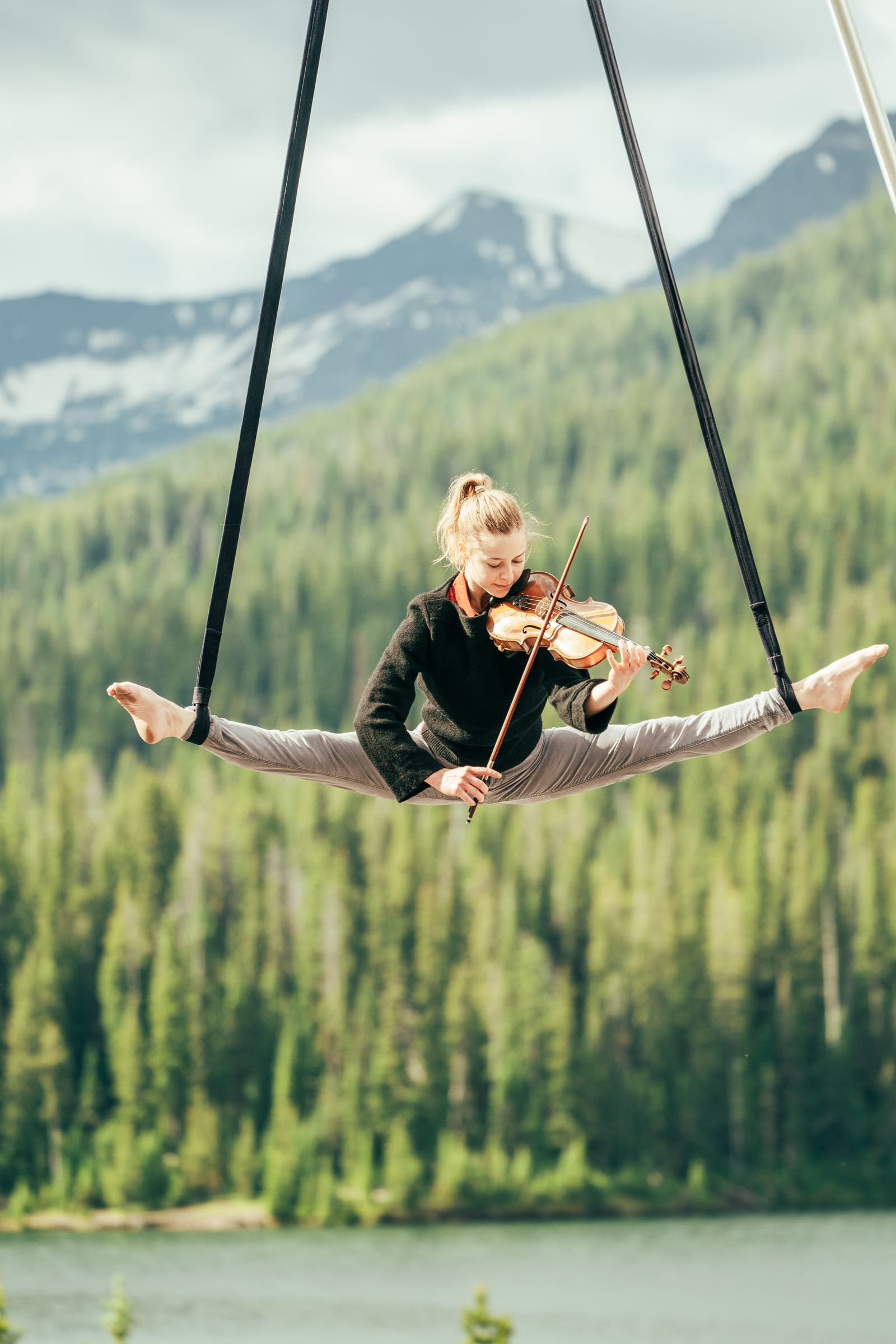 Aerial violinist suspended over alpine lake and forest